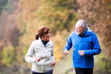 Beautiful active senior couple running together outside in sunny autumn nature