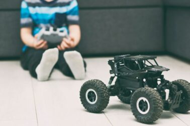 The boy is holding the joystick and plays with the radio control car