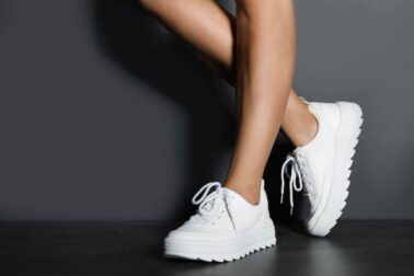 Woman in stylish sneakers near grey wall, closeup